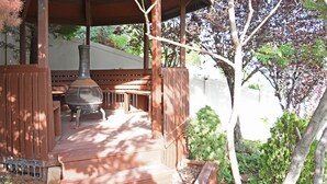 A covered outdoor area with a grill, wooden deck, and surrounding greenery.