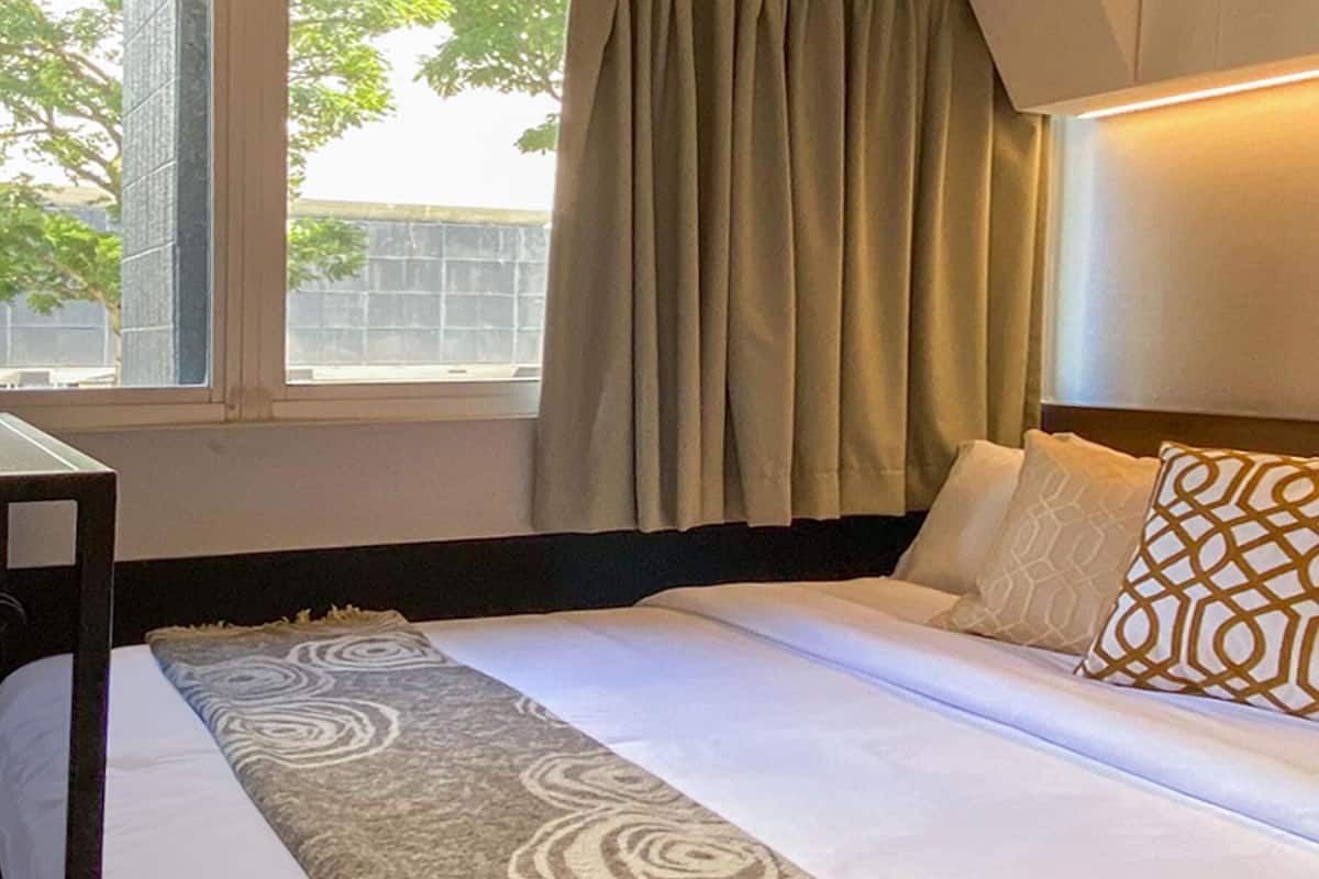 A hotel room with a bed, a small table, and a window with curtains.