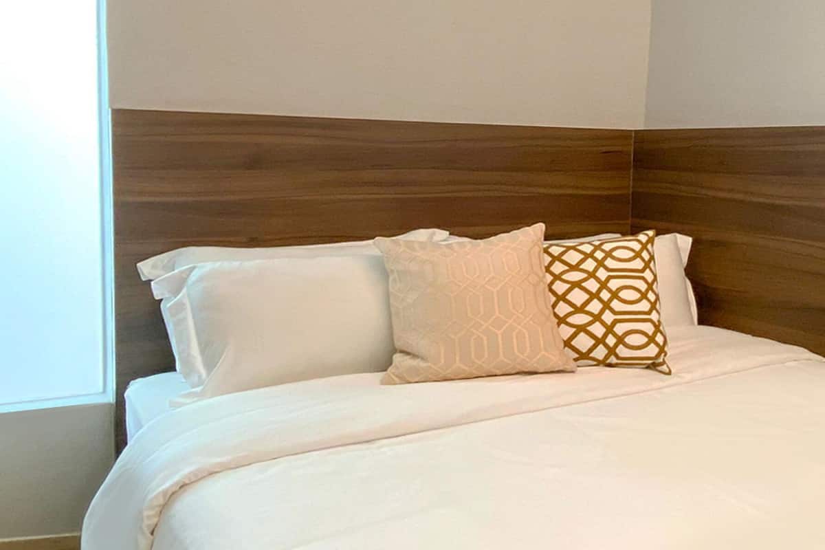A neatly made bed with white bedding and two decorative pillows, one with a geometric pattern.
