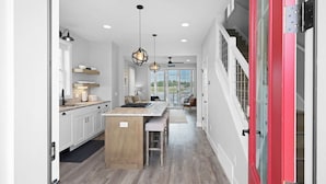 Ett modernt kök med en central köksö, hängande lampor och utsikt mot omgivningen.