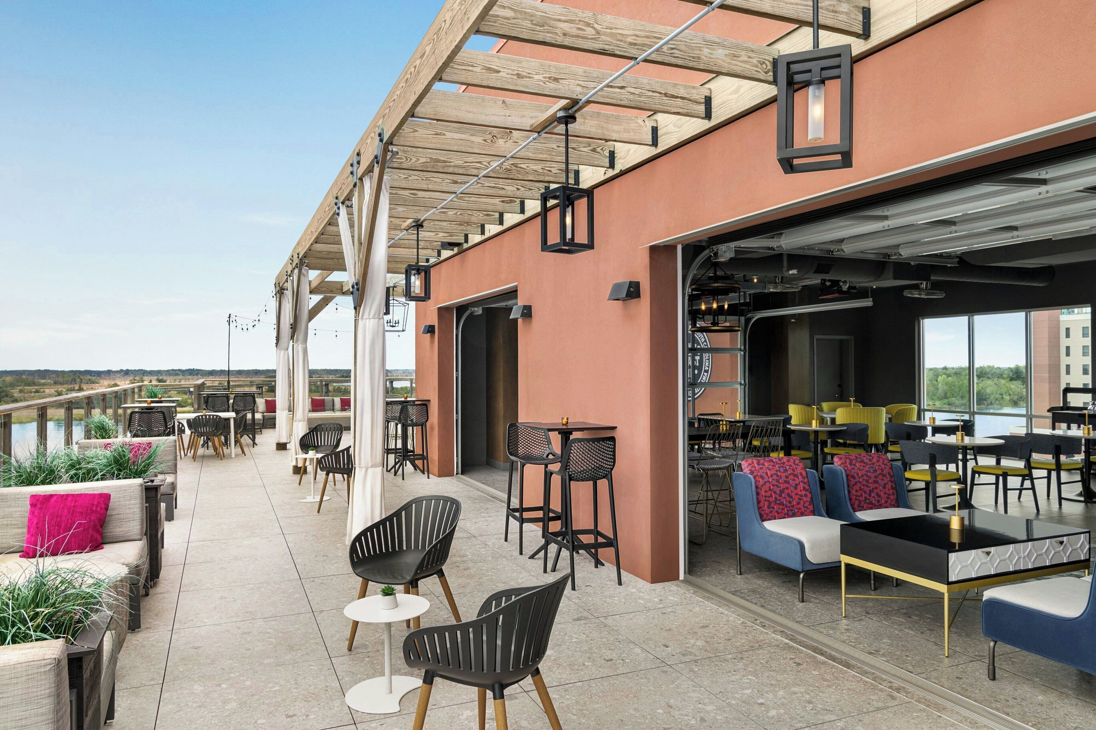 An outdoor patio area with seating and tables, a covered section with a bar, and a view of the landscape.