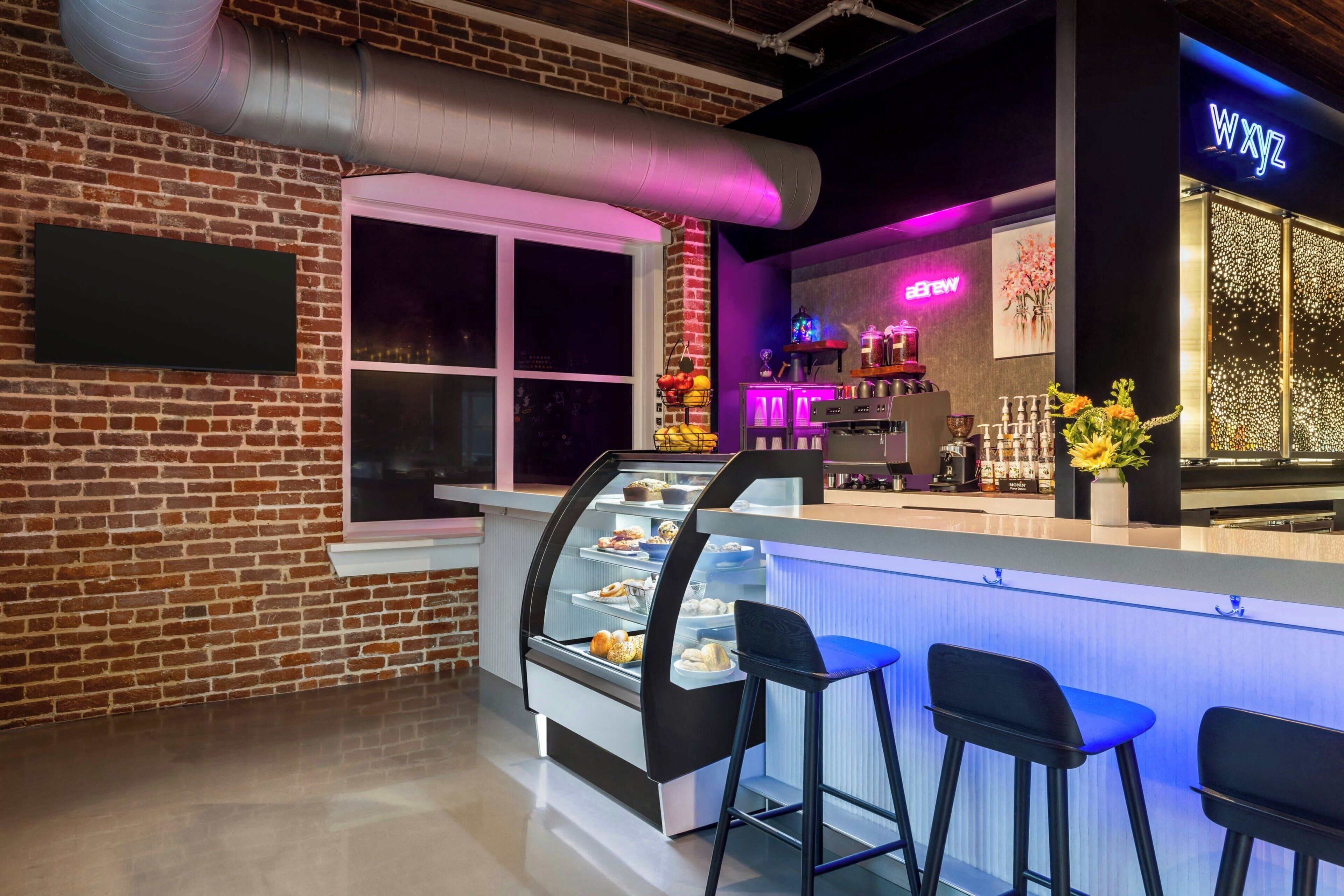 A modern bar area with a brick wall, a glass display case with food items, and a neon sign.