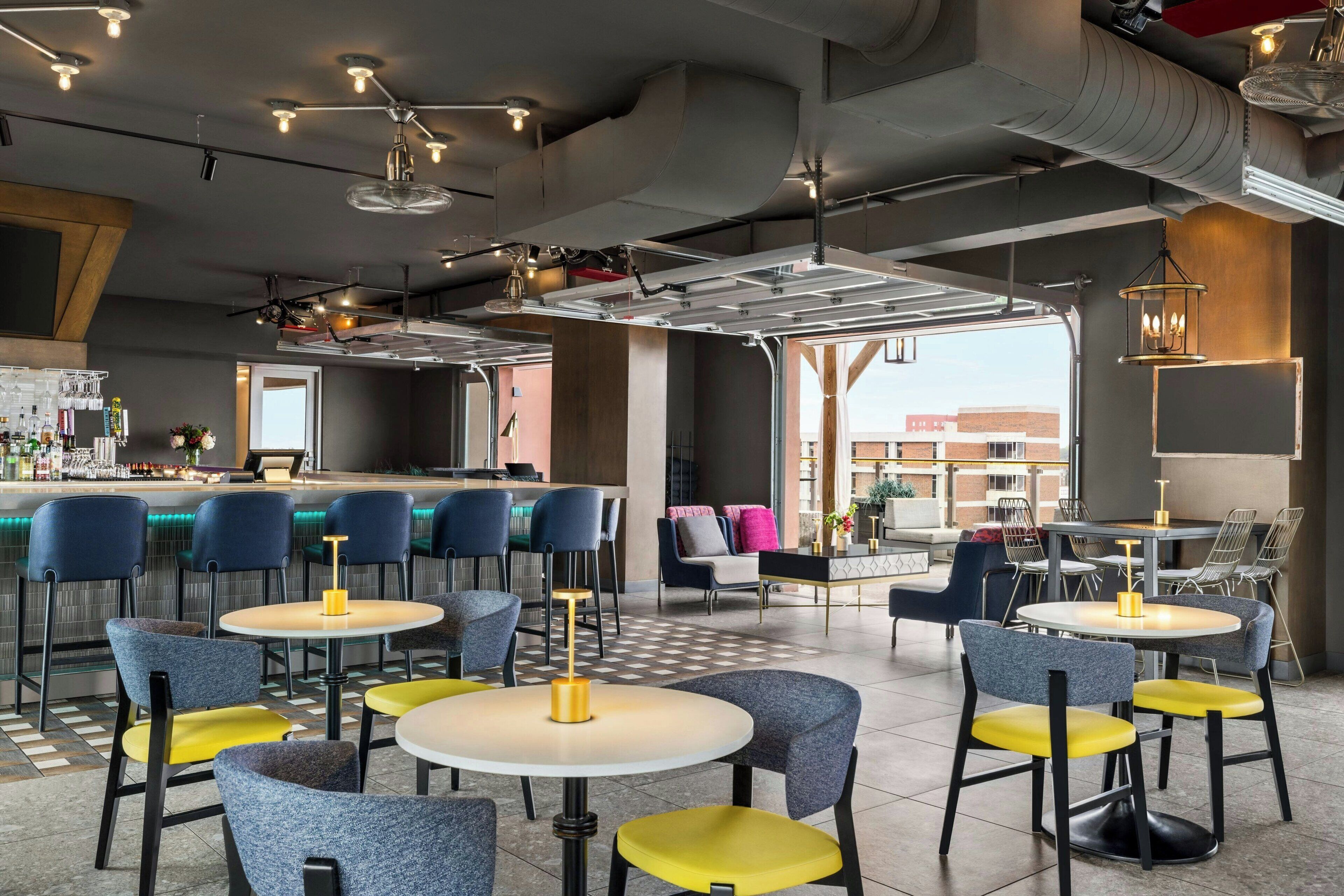 Ein modernes Restaurant mit runden Tischen und Stühlen, einer Bar und Blick auf die Stadt.