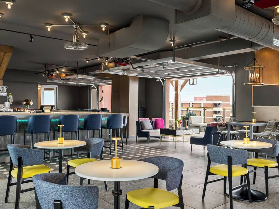 Ein modernes Restaurant mit runden Tischen und Stühlen, einer Bar und Blick auf die Stadt.