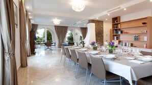 Un coin repas avec une longue table dressée pour le repas, des chaises, un lustre et une bibliothèque.