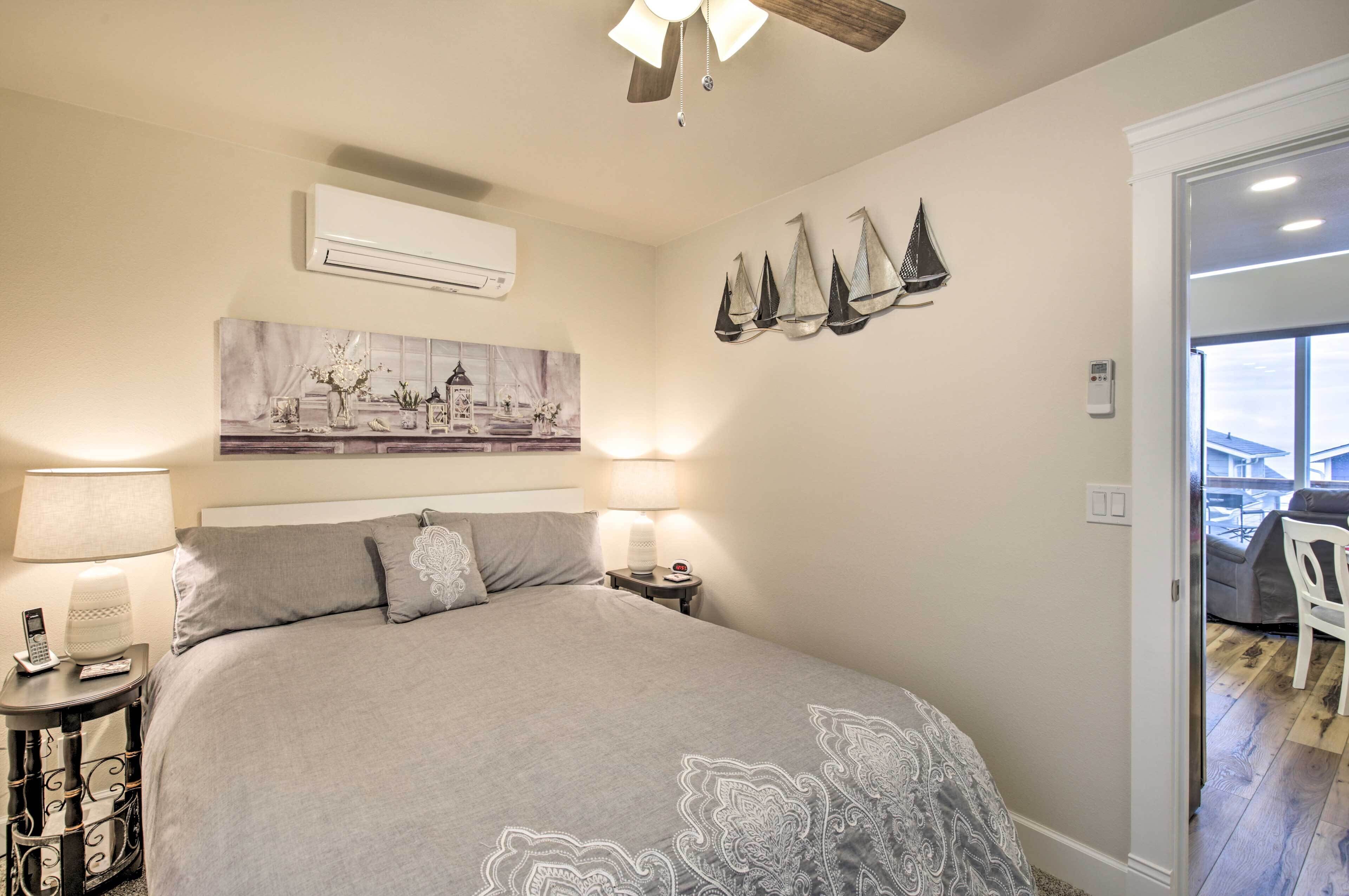 Un dormitorio con cama, lámparas de noche, aire acondicionado de pared, un cuadro y ventana con vistas.