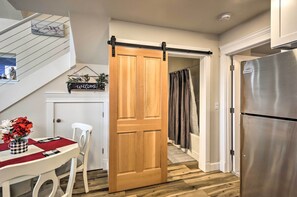 A kitchen with a sliding wooden door, a stainless steel refrigerator, a dining table with a red placemat, and a staircase leading to another room. - Peaceful Fall Escape: Oregon Home w/ Ocean View (Florence)