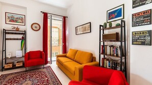 A living room with a sofa, a red armchair, a bookshelf, and a red curtain.