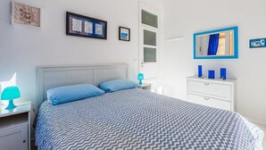 A bedroom with a bed, a nightstand, a dresser, and a window with curtains.