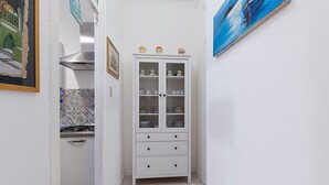 A narrow hallway with a white cabinet containing glassware, a tiled backsplash, and a painting on the wall.