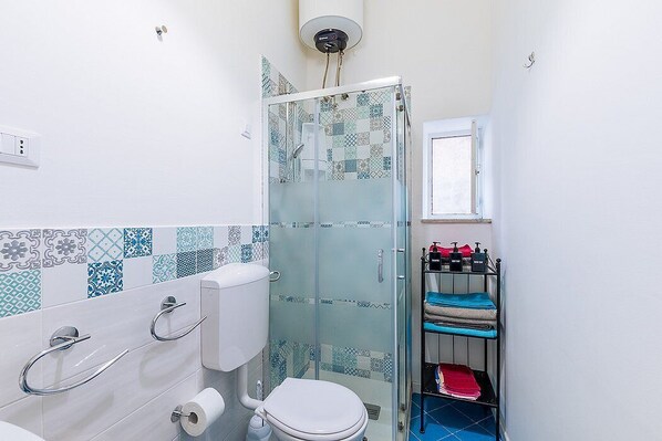 Un baño con inodoro, cabina de ducha de vidrio y repisa con artículos de aseo.