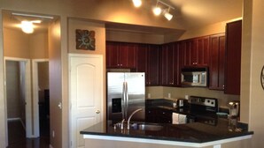 A kitchen with dark wooden cabinets, stainless steel appliances, and a central island with stools. - Beautiful centrally located townhome in The Gardens, Gilbert (Gilbert)