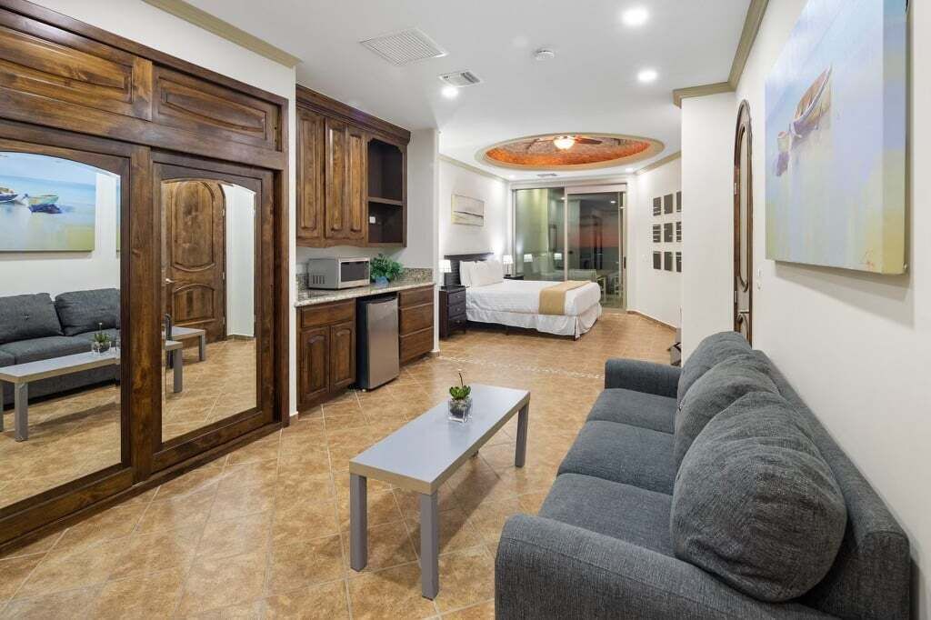 A modern living room with a grey sofa, a coffee table, and a kitchen area with wooden cabinets and a microwave.