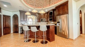 Una cocina con una isla central, taburetes de bar, un refrigerador de acero inoxidable y techo de ladrillo.