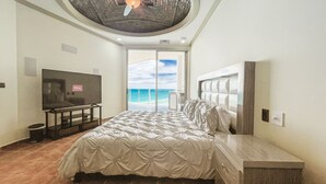 Un dormitorio con cama, televisor, vista al océano y techo de diseño único.