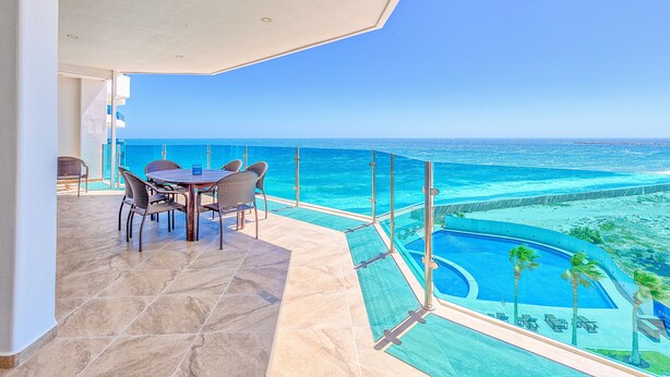 A balcony with a view of the ocean, a pool, and a dining area with chairs and a table. - Esmeralda Beach Resort 2 Bedrooms Condo B 502 (Puerto Peñasco)