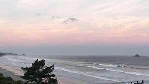 A coastal landscape with a beach, ocean waves, and distant islands under a cloudy sky. - Soothing Sounds (Otago)