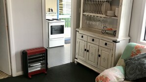 A compact living space with a kitchenette, a dining area with a white cabinet and shelves, a red fan, and a green patterned sofa. - Soothing Sounds (Otago)