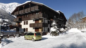 A multi-story chalet with balconies, a car parked in front, and snow-covered surroundings. - 3-room cabin apartment, south-facing balcony, 5 pers., private parking (Les Contamines-Montjoie)