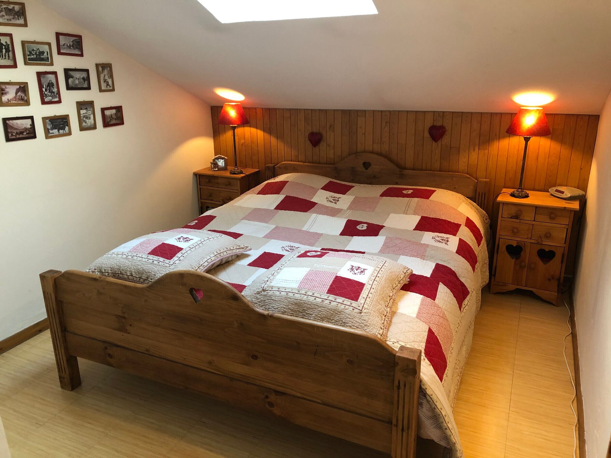 A bedroom with a wooden bed, a quilt, two bedside lamps, a nightstand, and a wall with framed pictures.