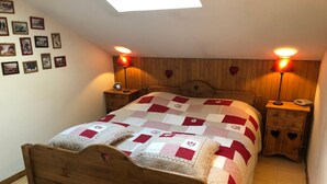 A bedroom with a wooden bed, a quilt, two bedside lamps, a nightstand, and a wall with framed pictures. - 3-room cabin apartment, south-facing balcony, 5 pers., private parking (Les Contamines-Montjoie)