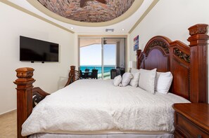 A bedroom with a large bed, a television, and a view of the ocean through a sliding door.