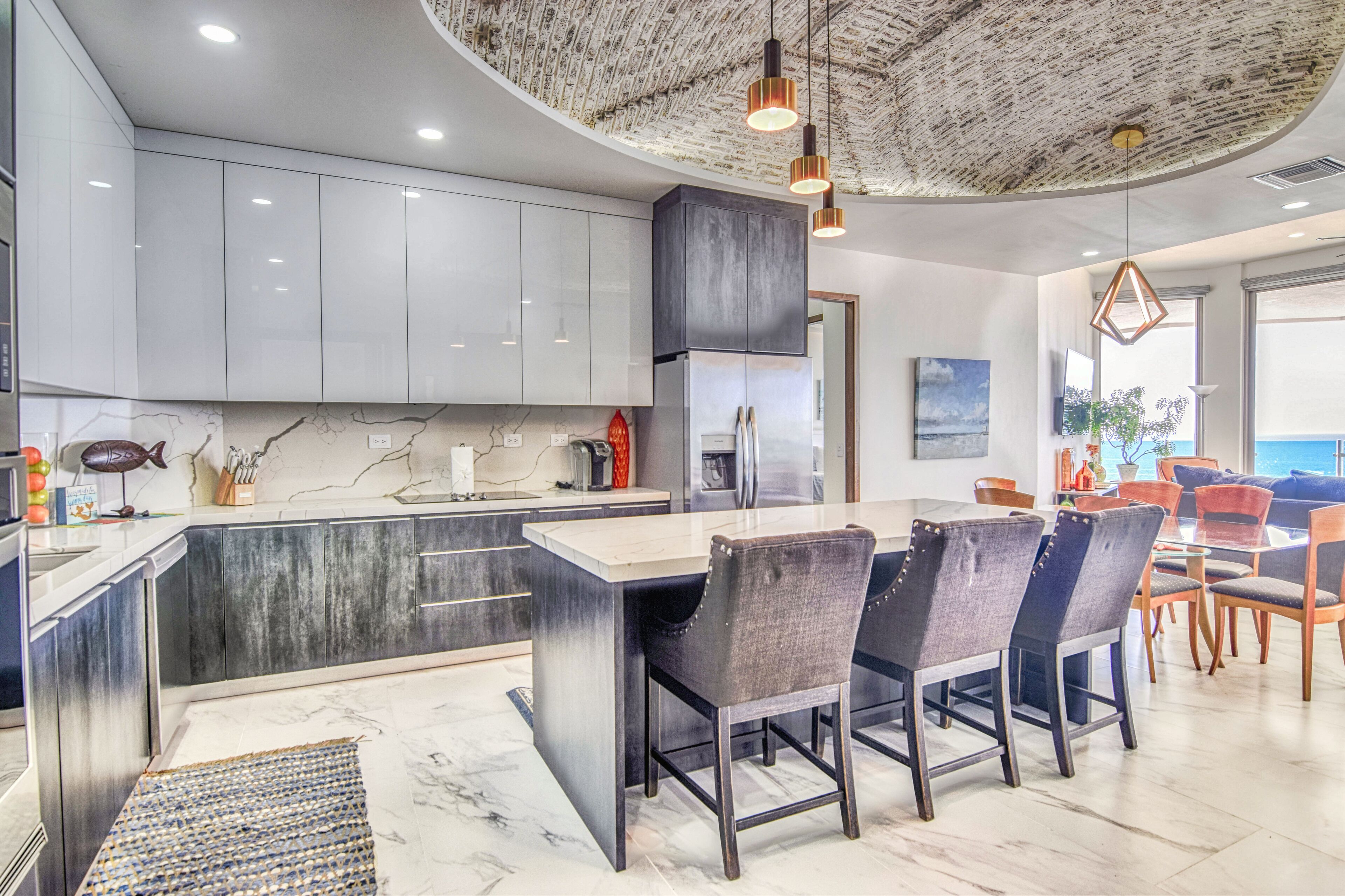 Een moderne keuken met een marmeren aanrecht, roestvrijstalen apparatuur en een eetgedeelte met een groot eiland en stoelen.