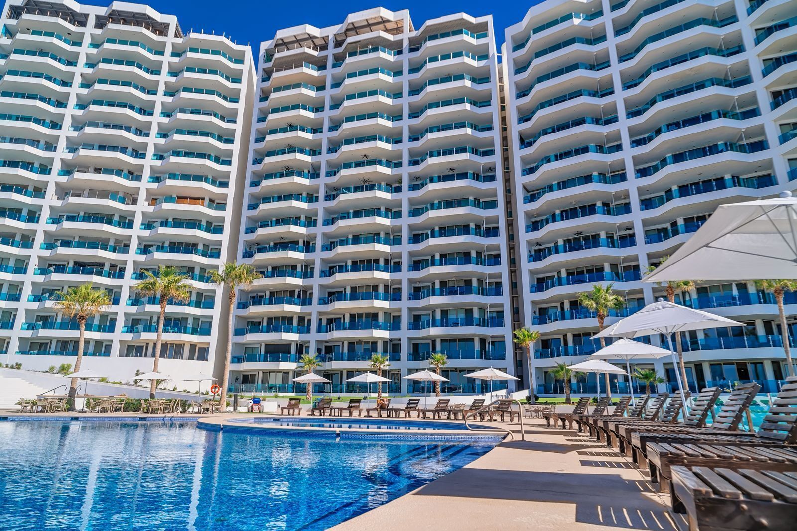 A high-rise hotel with multiple balconies, a swimming pool, and sun loungers.