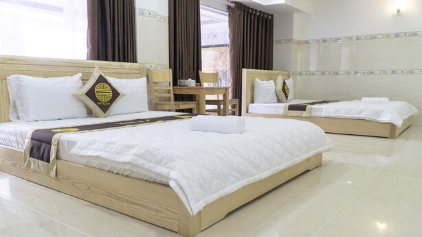A hotel room with two beds, a wooden headboard, a small table with chairs, and a window with curtains. - Dai An Binh Tan Hotel (Ho Chi Minh City)