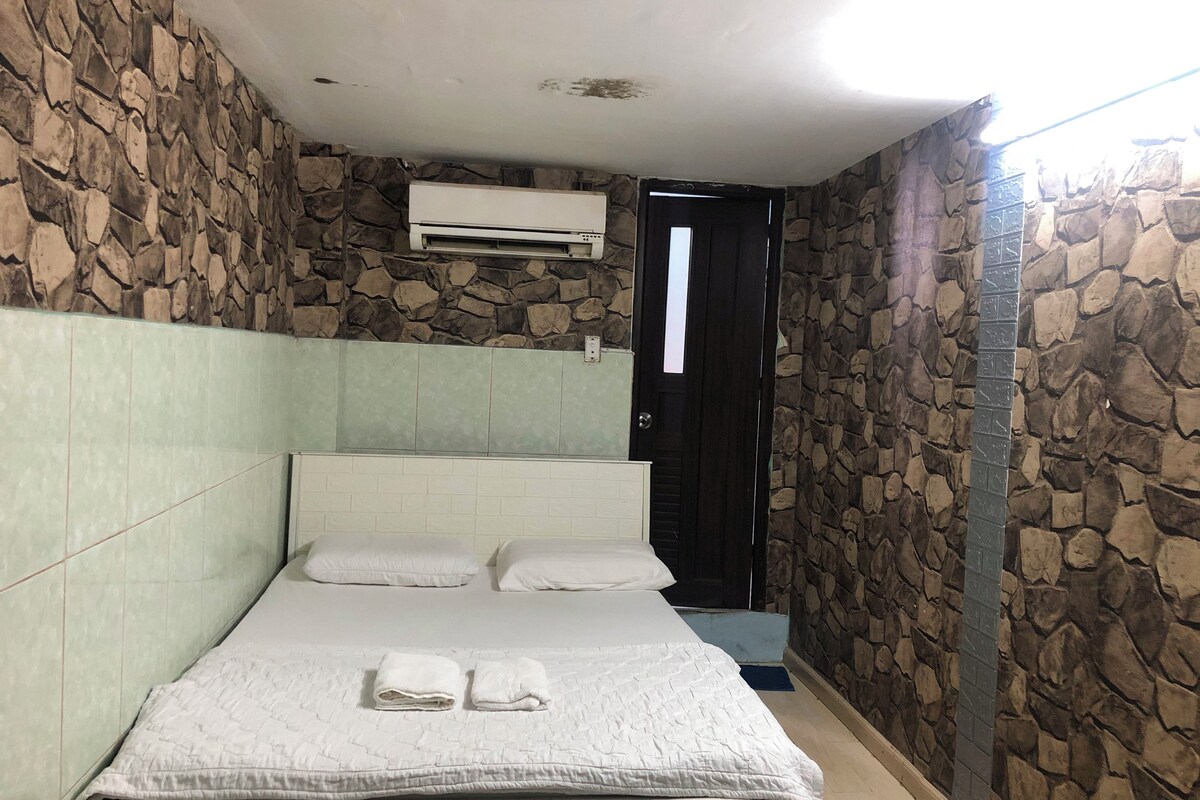 Een slaapkamer met een stenen muur, een bed met witte lakens en een aan de muur bevestigde airconditioning.