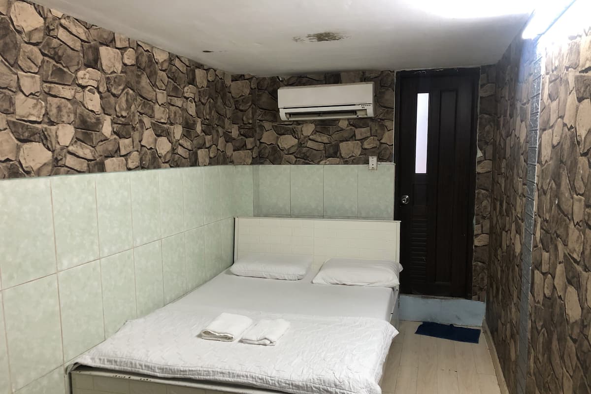 Quarto pequeno e estreito com uma cama, parede de pedra e unidade de ar condicionado.