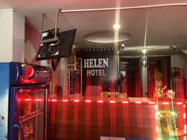 Interior de hotel com uma máquina de vendas automática, luzes de neon e uma placa indicando o Hotel Helen.