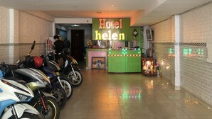 Eine Hotelhalle mit einer Rezeption, einem Schild mit der Aufschrift 'Hotel Helen' und mehreren Motorrädern im Hintergrund.