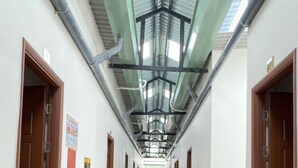 Un pasillo con baldosas estampadas en el suelo, vigas metálicas en el techo y puertas de madera a ambos lados.