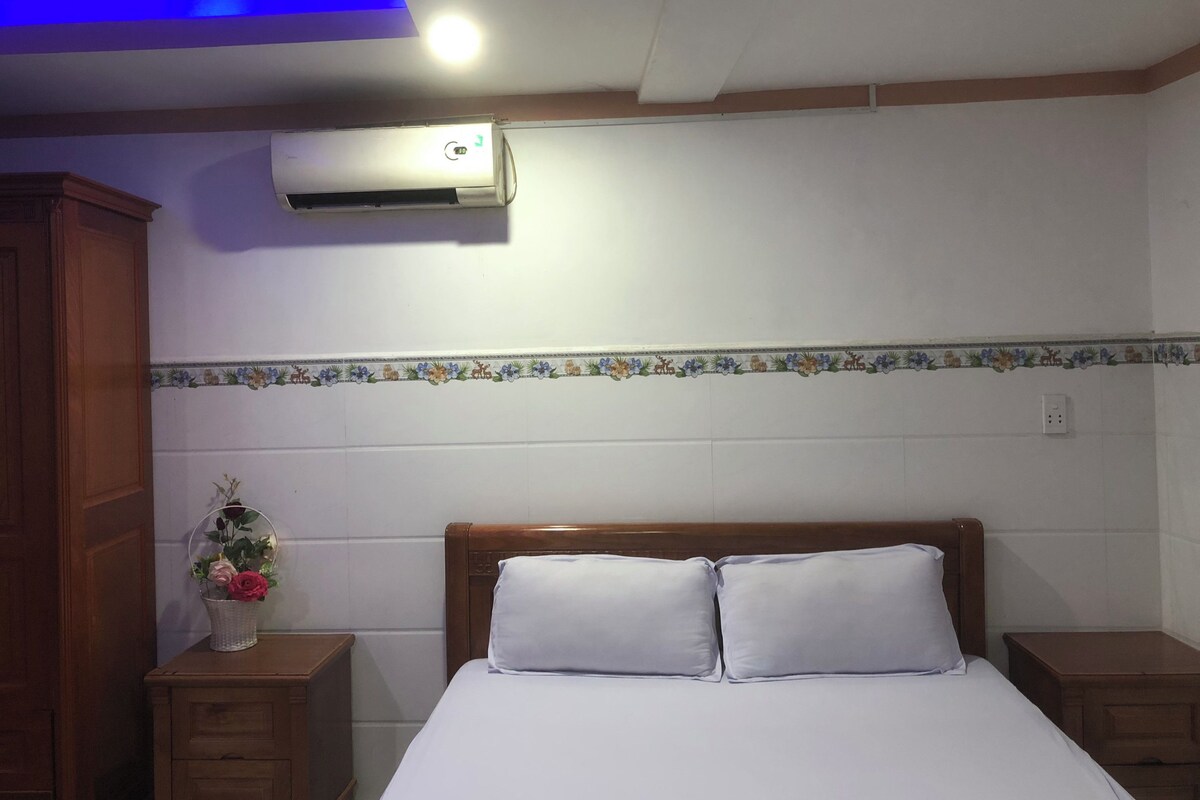 Une chambre à coucher avec un lit, des tables de chevet en bois, un vase décoratif et un appareil de climatisation.
