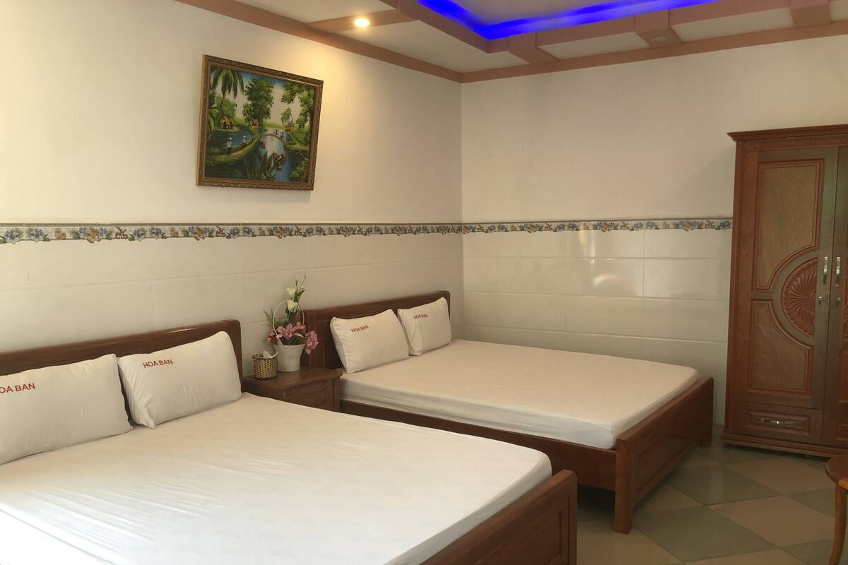 A hotel room with two wooden beds, a nightstand with a basket and flowers, a wooden wardrobe, and a painting on the wall.