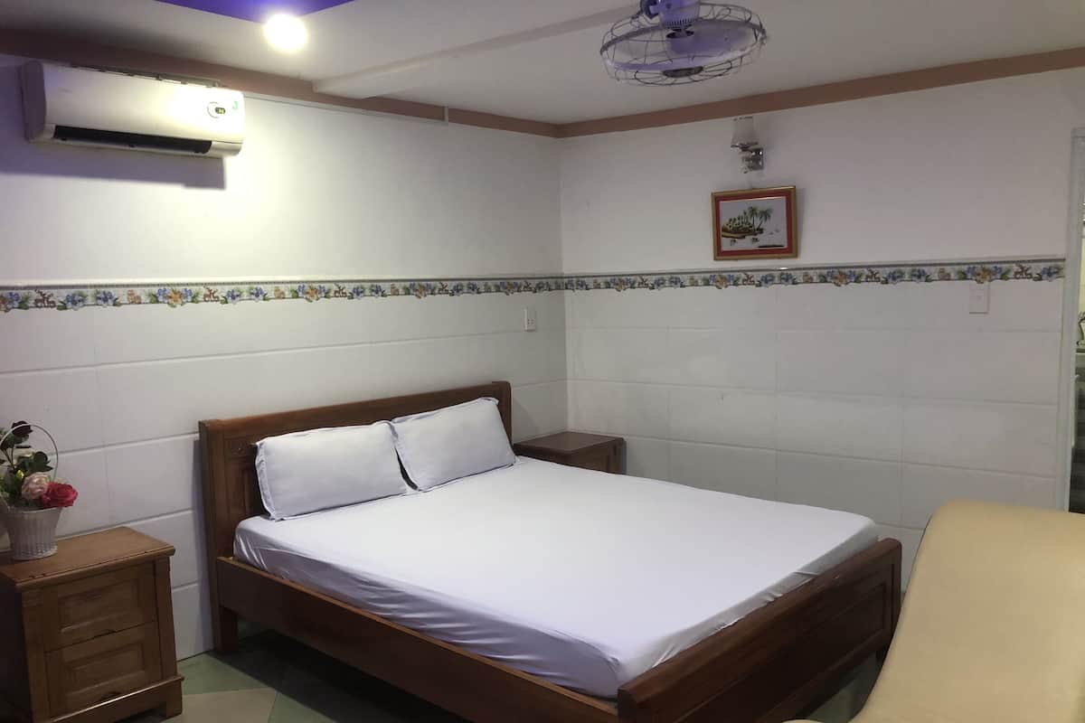 A bedroom with a wooden bed, white bedding, a nightstand with a lamp, a small table with a vase of flowers, and a ceiling fan.