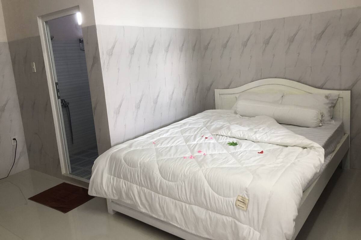 A bedroom with a bed, a door leading to a bathroom, and a marble-patterned wall.