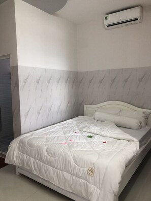 A bedroom with a bed, white bedding, a marble-patterned wall, and an air conditioning unit. - Duc Linh Hotel (Phu Quoc)