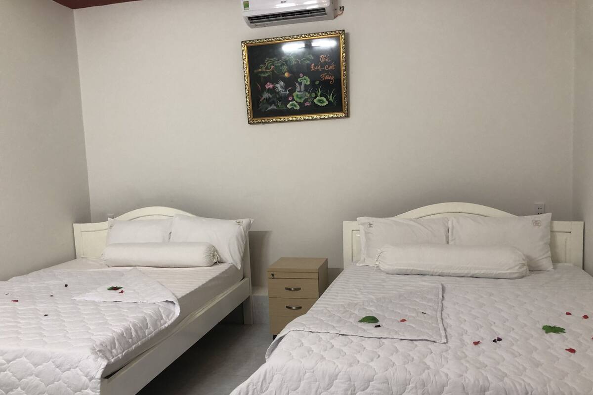 A bedroom with two beds, each with white bedding and pillows, a small wooden nightstand, and a framed picture on the wall.