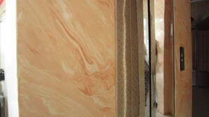 Una pared de mármol con un patrón texturizado, una puerta de ascensor metálica y un panel de vidrio.