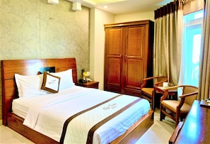 A hotel room with a large bed, wooden wardrobe, a desk, and a chair.