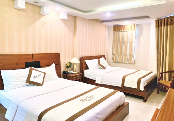 A hotel room with two beds, each with a wooden headboard, white bedding, and a brown decorative trim. There is a nightstand with a lamp and a telephone on one bed, and a chair next to the other bed.