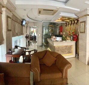 A hotel lobby with a reception desk, a dining area, and a seating area with sofas.