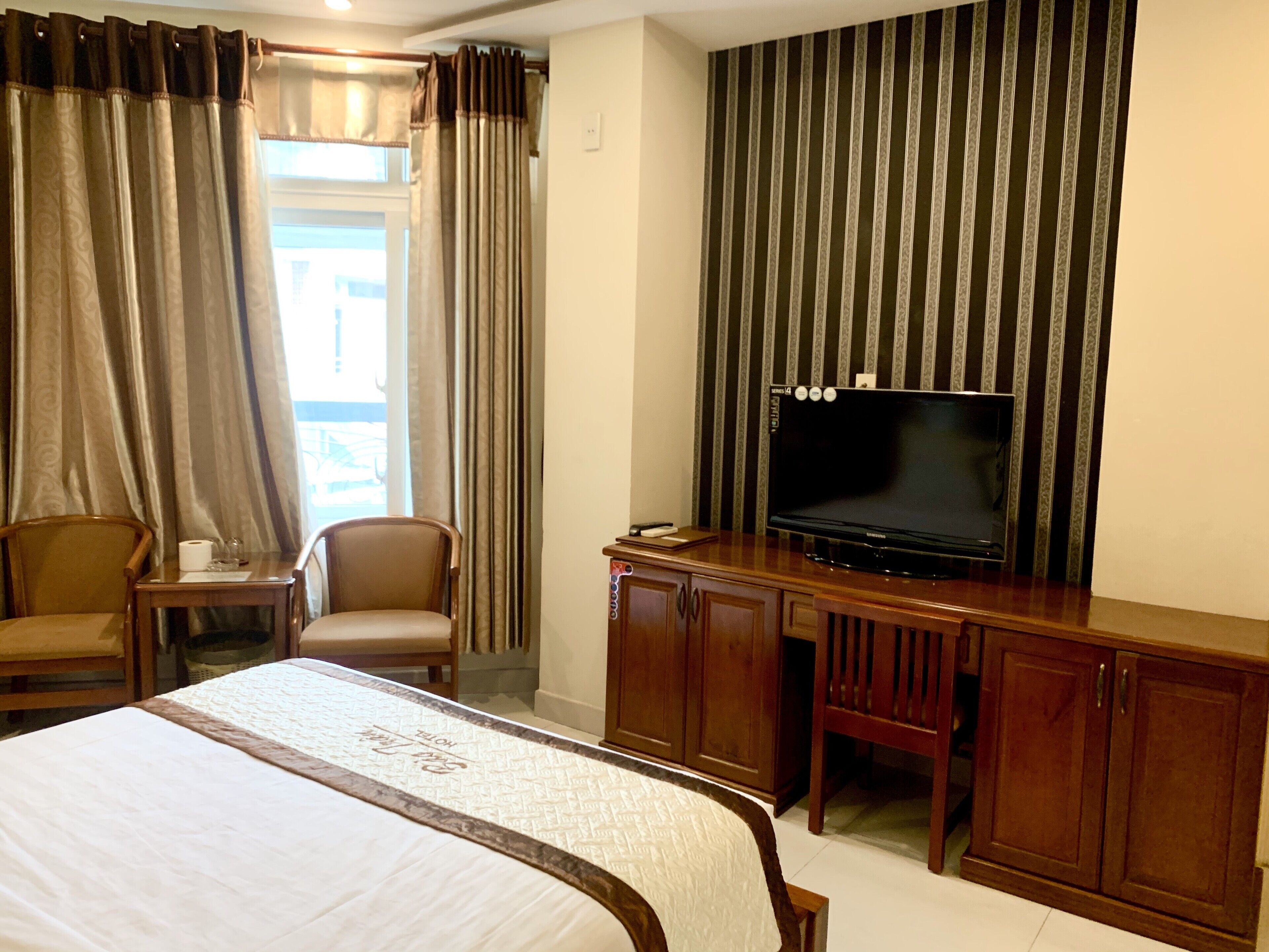 A hotel room with a bed, a desk, a chair, a television, and curtains.