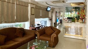 Eine großzügige Lobby mit zwei braunen Sofas, einem Glastisch und einer dekorativen Decke.