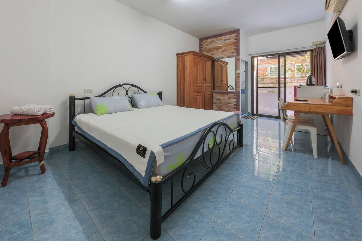 A bedroom with a bed, a wooden wardrobe, a desk, and a chair.