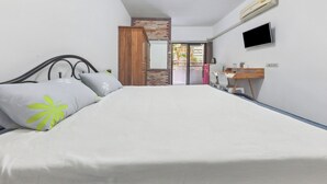 A bedroom with a bed, a wooden wardrobe, a desk with a chair, a flat-screen TV, and a sliding glass door leading to an outdoor area. - View Mansion (Chonburi)