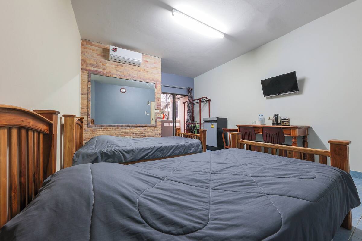 A hotel room with two beds, a desk with a chair, a TV, and a window with curtains.