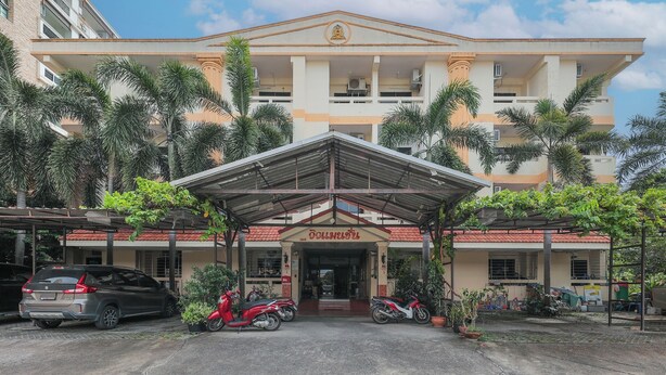 A building with a covered entrance, palm trees, and parked vehicles. - View Mansion (Chonburi)